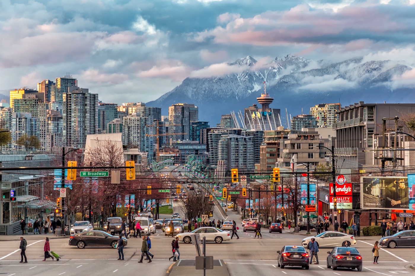 Busy West Broadway intersection in Vancouver with downtown towers and snow-dusted North Shore mountains behind